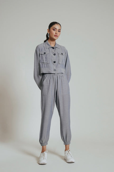 A woman modeling a grey co-ord set which includes a jacket and pants, paired with white sneakers.