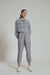 A woman modeling a grey co-ord set which includes a jacket and pants, paired with white sneakers.
